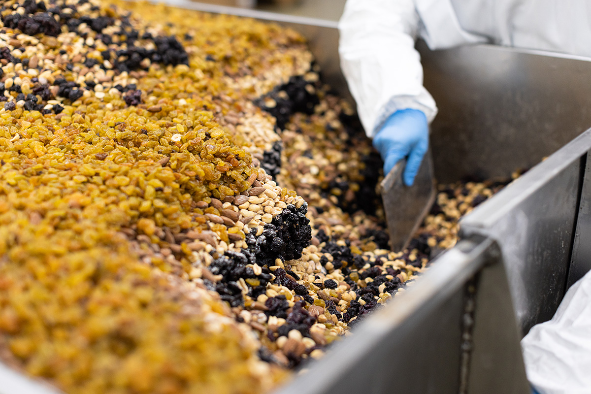 Employee mixing dried raisins, dried cranberries, peanuts, and almonds equally